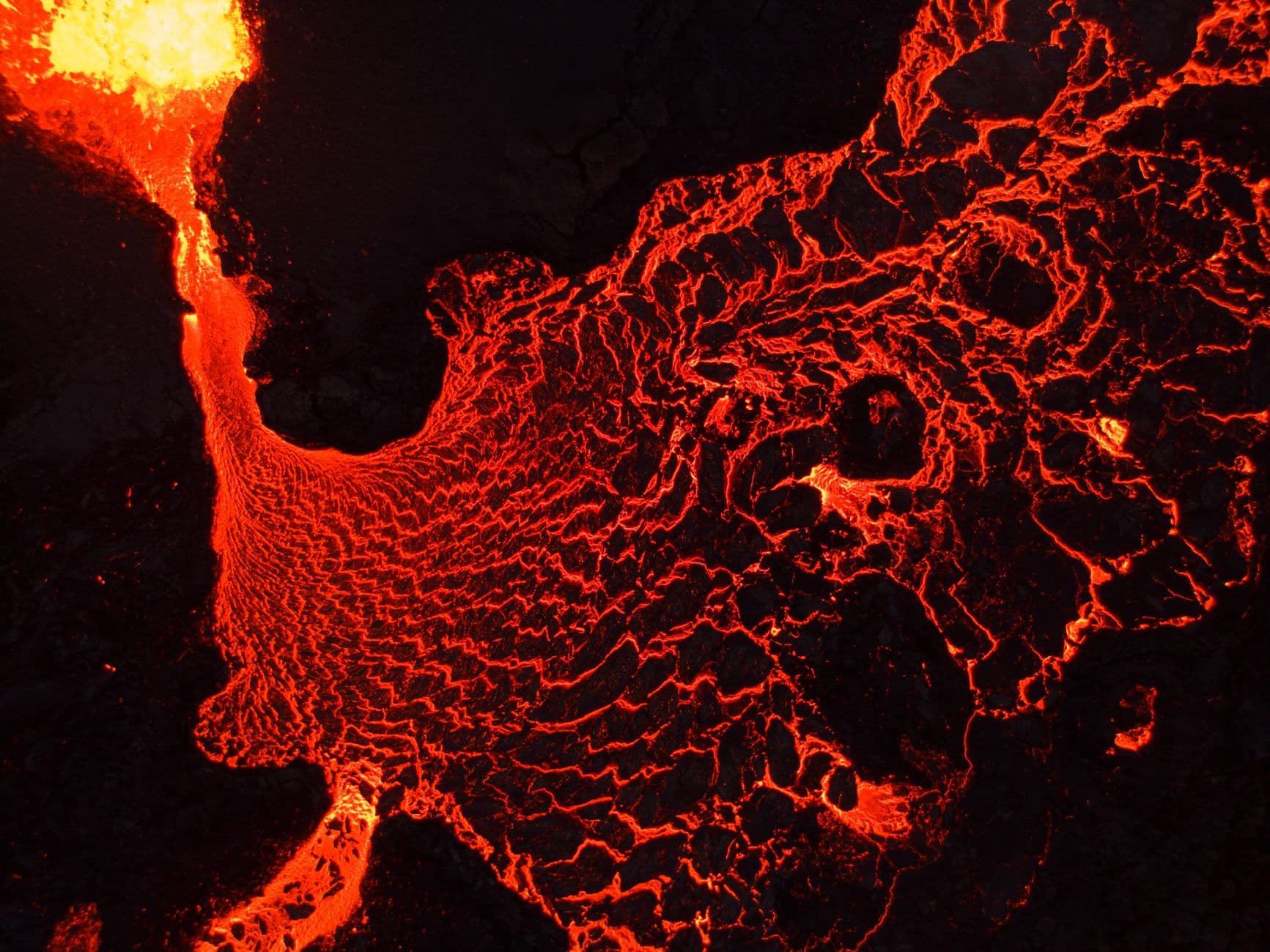 A breathtaking aerial view of flowing lava, showcasing vibrant red hues and geological textures.
