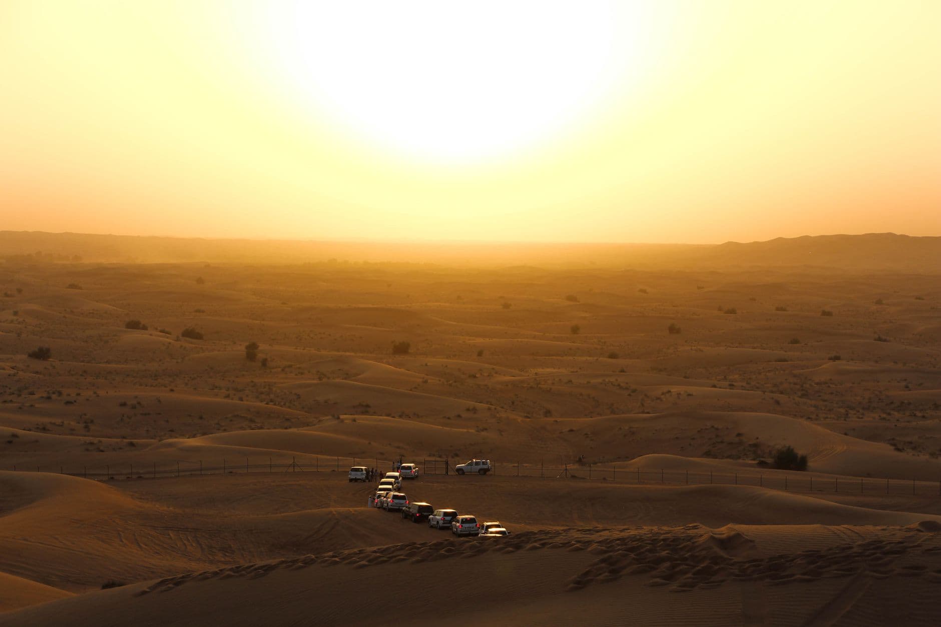 Off-road vehicles traverse the desert dunes under a warm golden sunset, ideal for adventure travel.