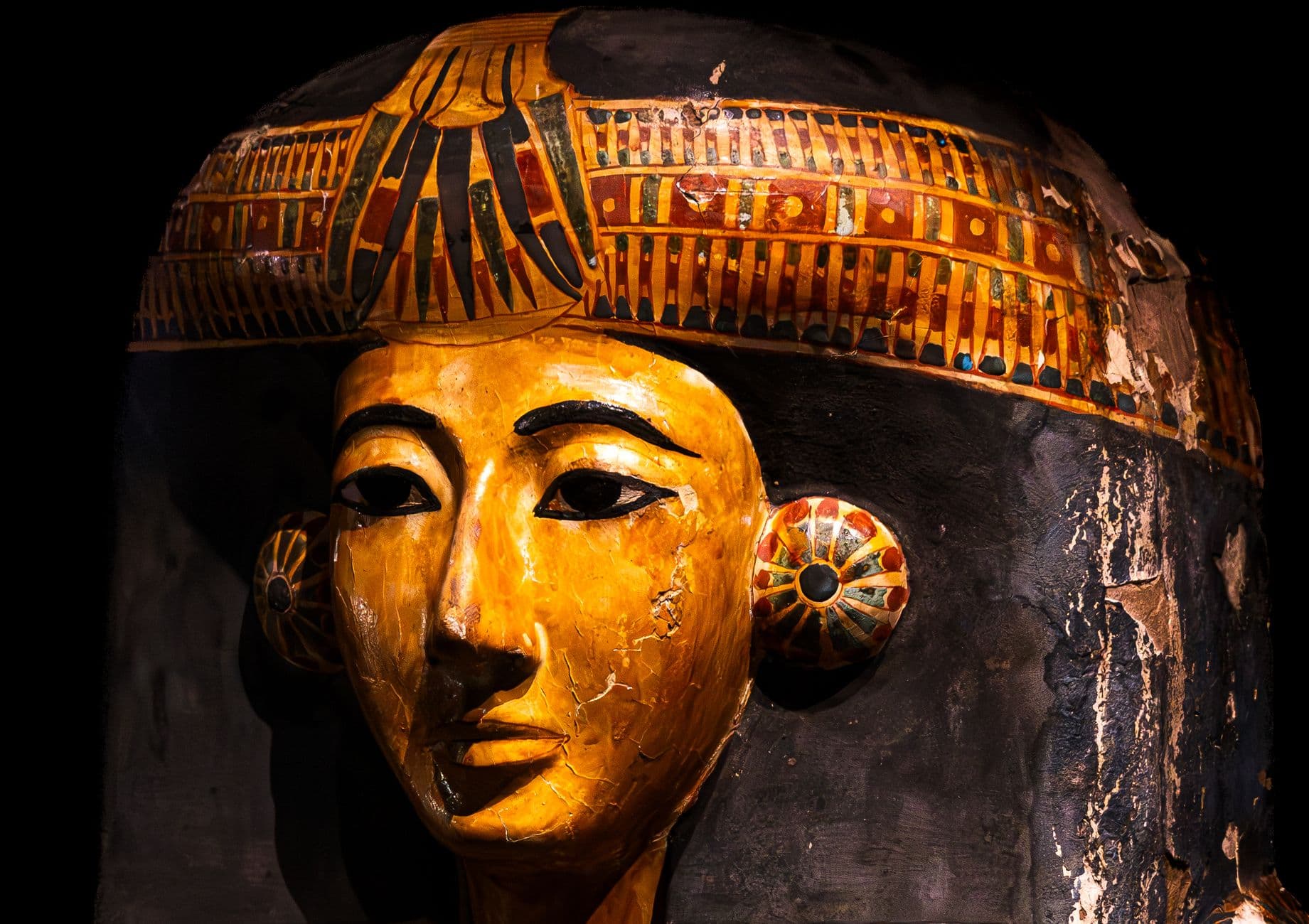 Detailed view of an ancient Egyptian sarcophagus mask with vibrant colors in a museum.