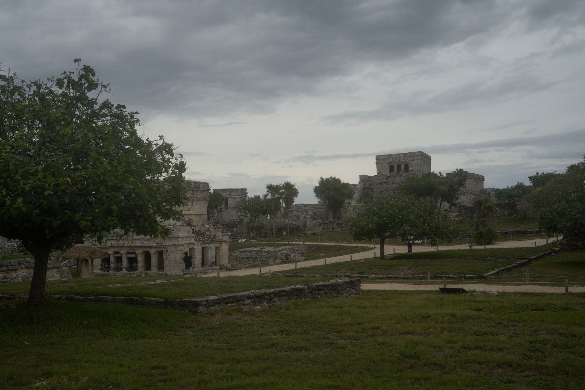Explore the historic ruins of Tulum in Mexico surrounded by lush trees and overcast skies.
