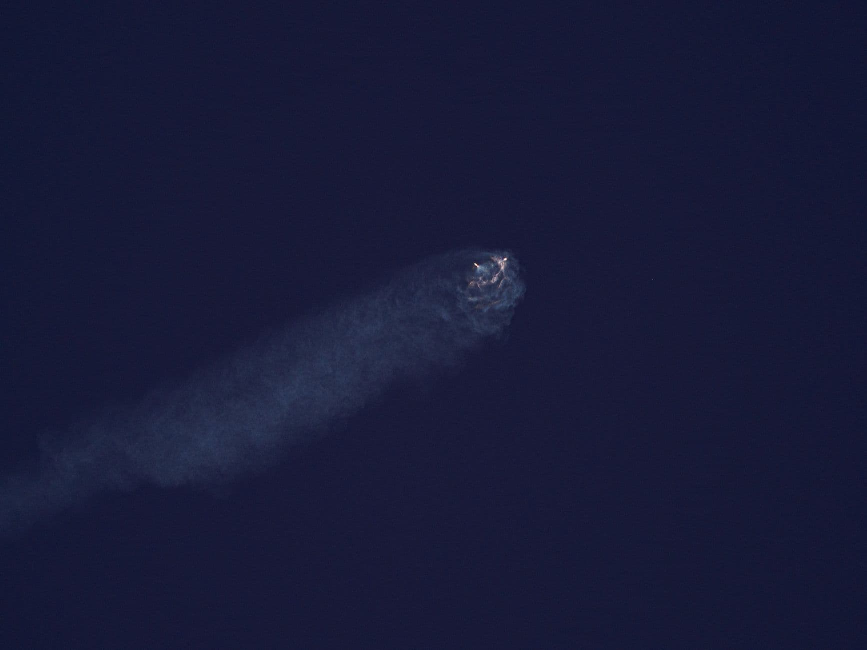 Bright celestial body streaks through dark night sky leaving a smoky trail.